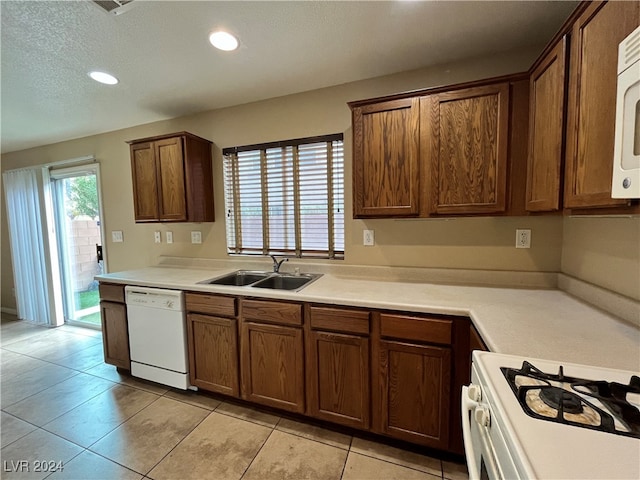 kitchen with white appliances, light tile patterned floors, a textured ceiling, and sink