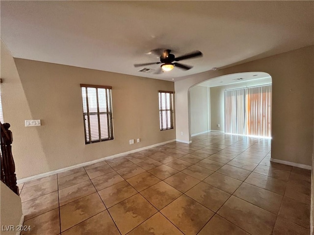 unfurnished room with arched walkways, light tile patterned floors, visible vents, ceiling fan, and baseboards