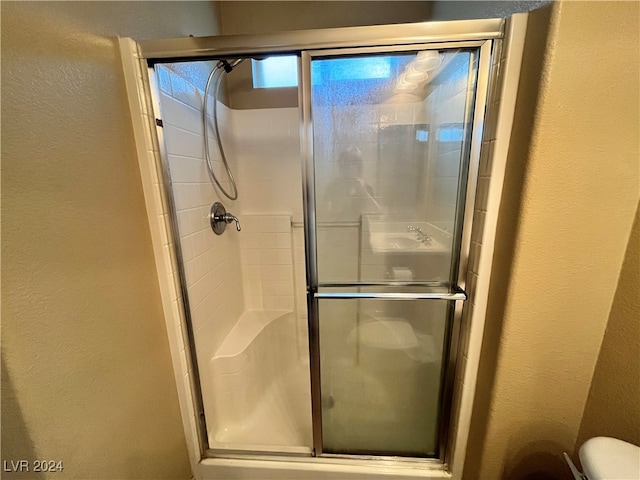 bathroom featuring a shower with door and toilet