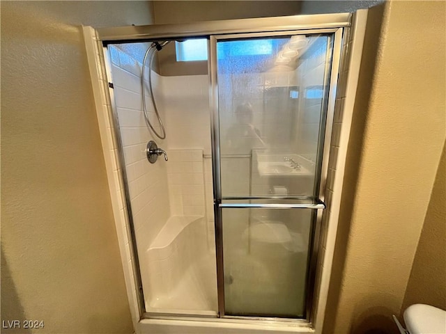 bathroom featuring toilet, a shower stall, and a textured wall