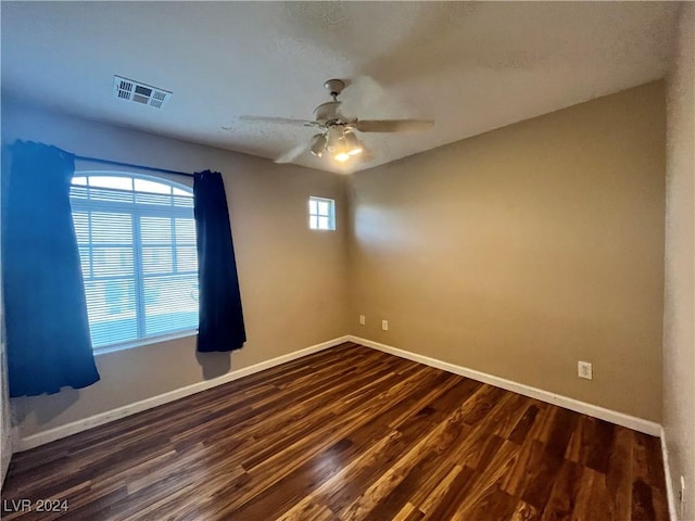 spare room featuring ceiling fan, dark wood finished floors, visible vents, and baseboards