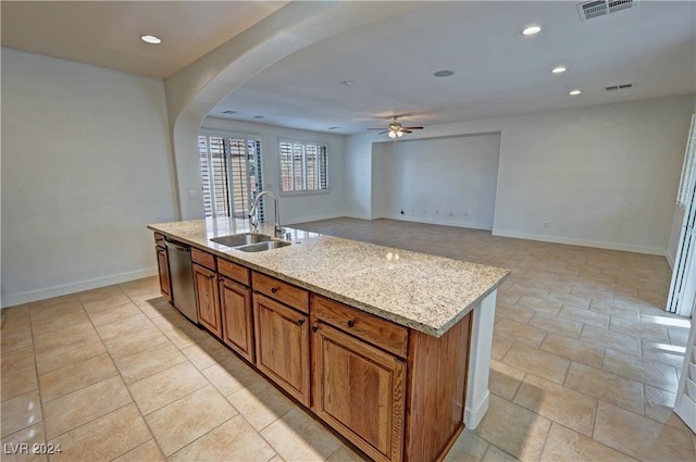 kitchen featuring a kitchen island with sink, sink, light stone countertops, stainless steel dishwasher, and ceiling fan