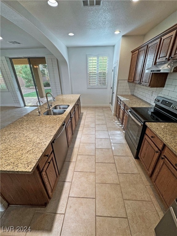 kitchen featuring a center island with sink, backsplash, light stone countertops, sink, and stainless steel appliances