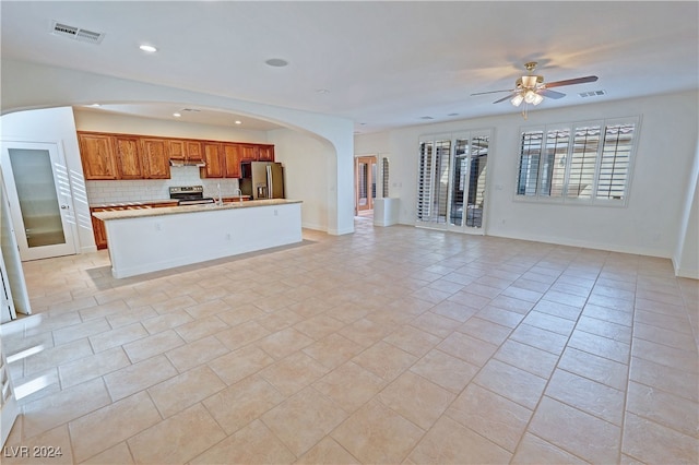 kitchen featuring appliances with stainless steel finishes, an island with sink, backsplash, and light tile patterned flooring