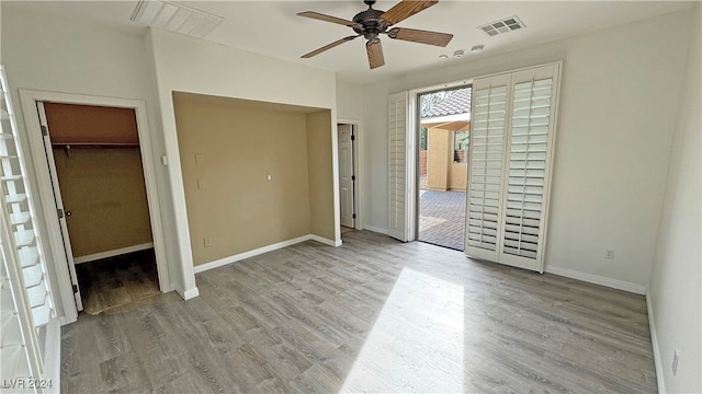 unfurnished bedroom with a closet, ceiling fan, light wood-type flooring, and a walk in closet