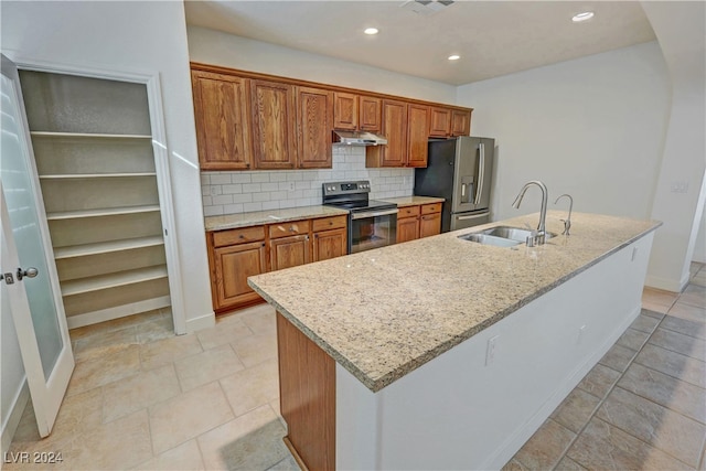 kitchen with decorative backsplash, an island with sink, sink, light stone countertops, and appliances with stainless steel finishes