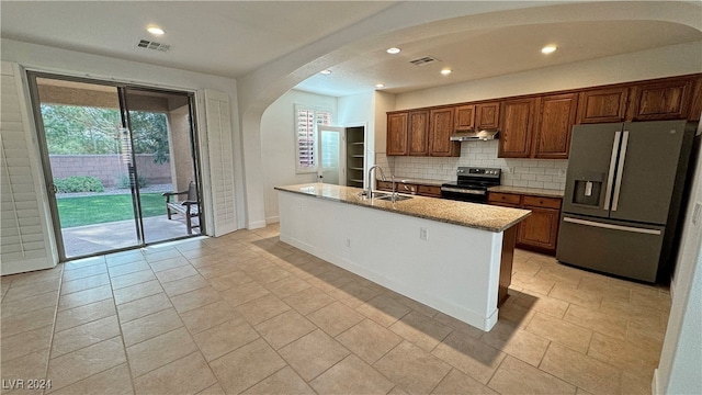 kitchen featuring decorative backsplash, a kitchen island with sink, sink, light stone countertops, and appliances with stainless steel finishes