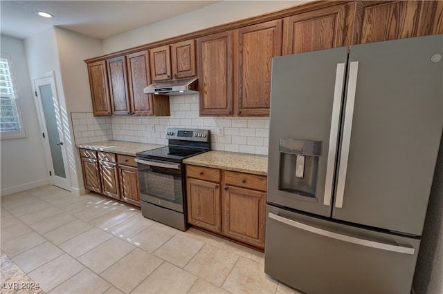 kitchen with light stone countertops, appliances with stainless steel finishes, backsplash, and light tile patterned flooring