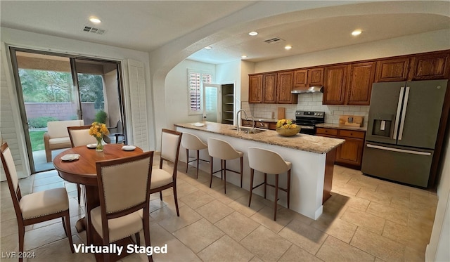 kitchen with tasteful backsplash, sink, an island with sink, stainless steel appliances, and light stone counters