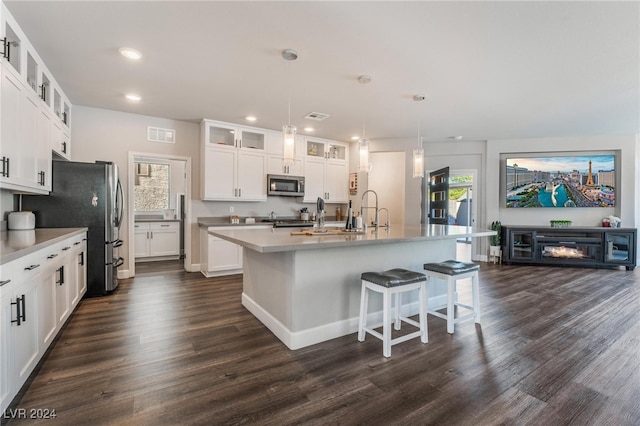 kitchen with a kitchen island with sink, dark wood-type flooring, stainless steel appliances, pendant lighting, and white cabinetry