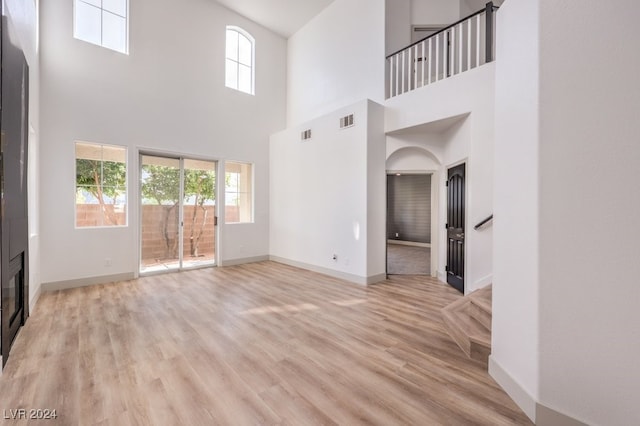 unfurnished living room featuring a high ceiling and light hardwood / wood-style flooring