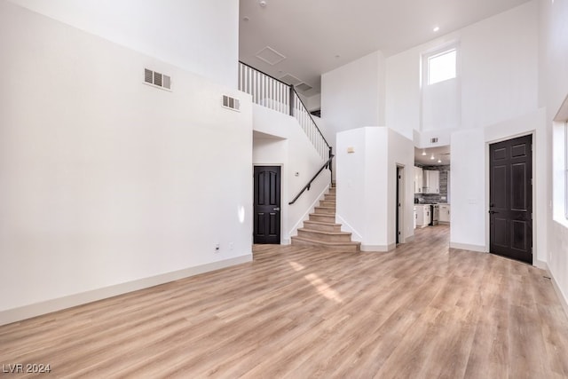 unfurnished living room featuring a towering ceiling and light wood-type flooring