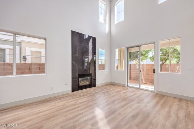 unfurnished living room with a towering ceiling, a tile fireplace, and light wood-type flooring