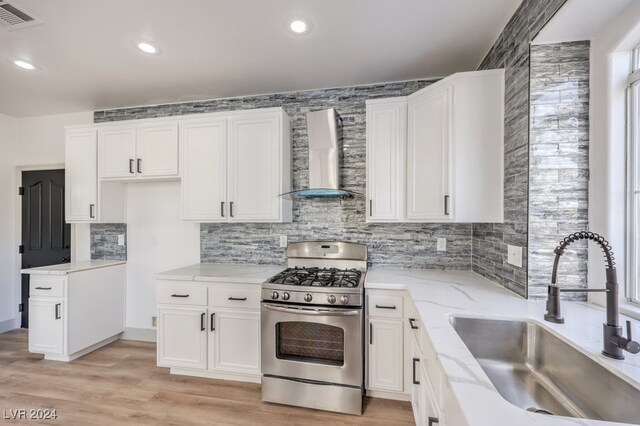 kitchen featuring sink, white cabinetry, light hardwood / wood-style floors, wall chimney exhaust hood, and gas range