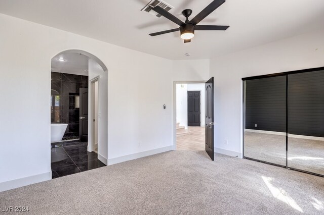 unfurnished bedroom with a closet, ceiling fan, connected bathroom, and dark colored carpet