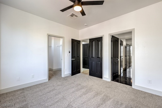 unfurnished bedroom featuring a walk in closet, carpet floors, a closet, and ceiling fan