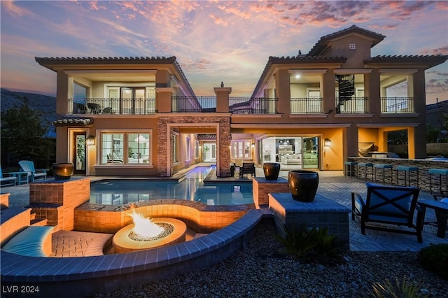 back house at dusk with a patio, a balcony, and a fire pit