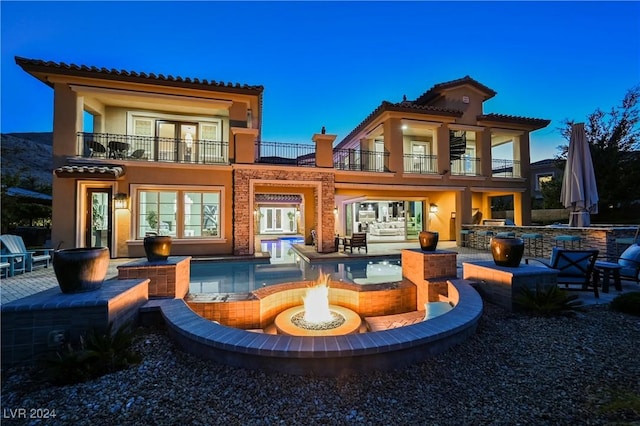 back house at dusk featuring a fire pit, a patio area, and a balcony