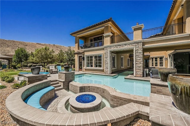 back of house with a swimming pool with hot tub, a balcony, a fire pit, and a patio area