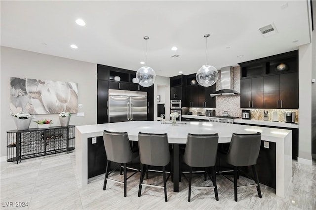 kitchen featuring pendant lighting, a center island with sink, wall chimney exhaust hood, tasteful backsplash, and stainless steel appliances