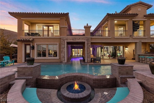 back house at dusk featuring a fire pit, a patio area, and a balcony