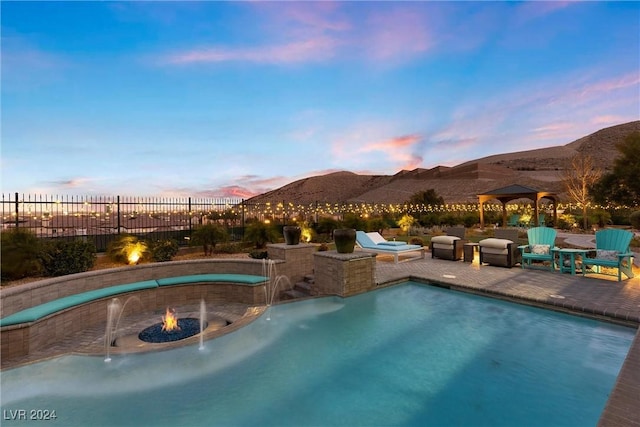 pool at dusk featuring pool water feature, a mountain view, a patio area, and a gazebo