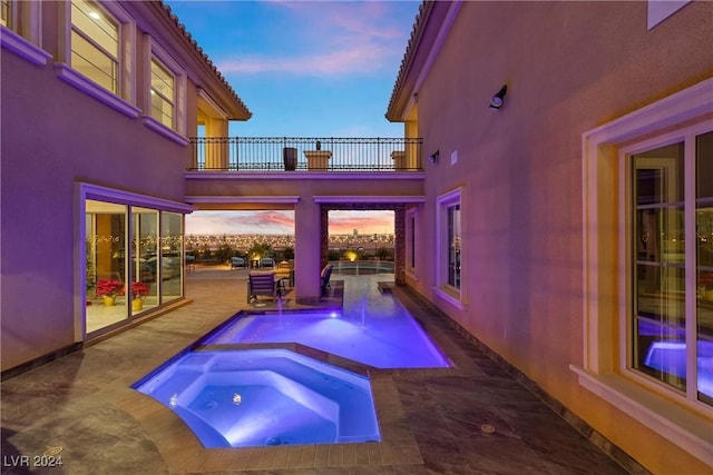 pool at dusk featuring an in ground hot tub and a patio