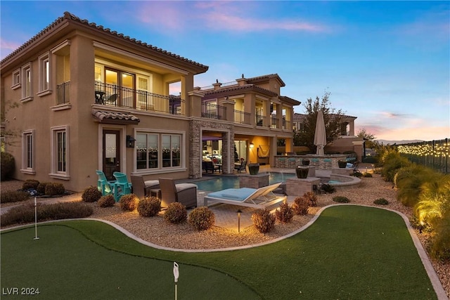 back house at dusk with a patio area, a swimming pool with hot tub, and a balcony