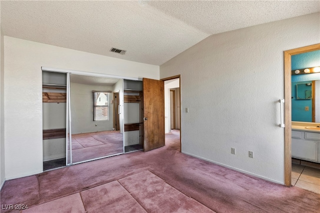 unfurnished bedroom with lofted ceiling, a textured ceiling, connected bathroom, carpet floors, and a closet