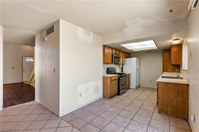 kitchen with a textured ceiling, appliances with stainless steel finishes, sink, and light tile patterned flooring