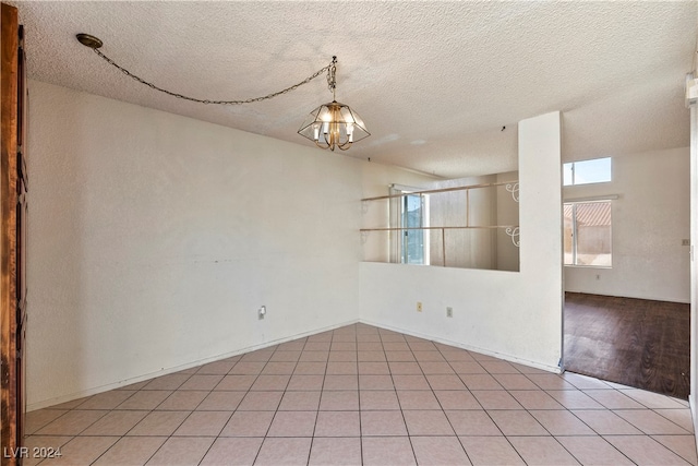 tiled spare room featuring a notable chandelier and a textured ceiling