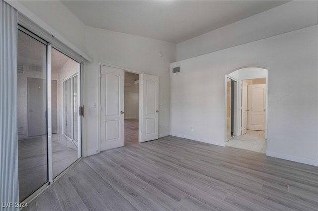 unfurnished bedroom with ensuite bathroom, a closet, and light hardwood / wood-style flooring