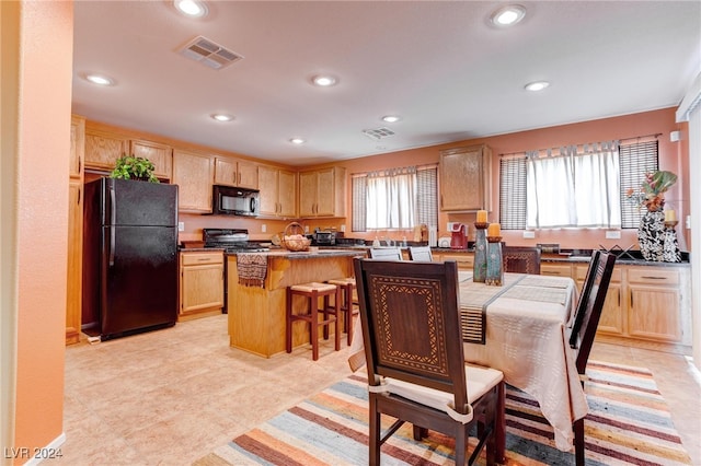 kitchen featuring a center island, black appliances, light brown cabinetry, and a breakfast bar area