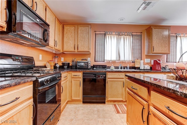 kitchen with dark stone counters, sink, black appliances, light tile patterned floors, and light brown cabinetry