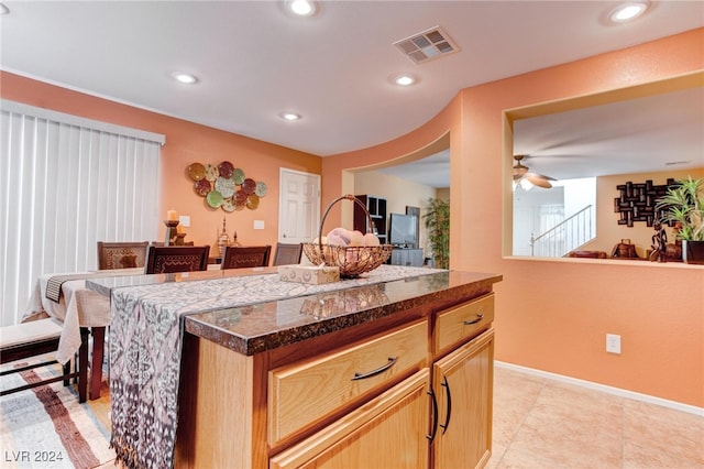 kitchen with a kitchen island, light brown cabinets, a kitchen bar, light tile patterned floors, and ceiling fan