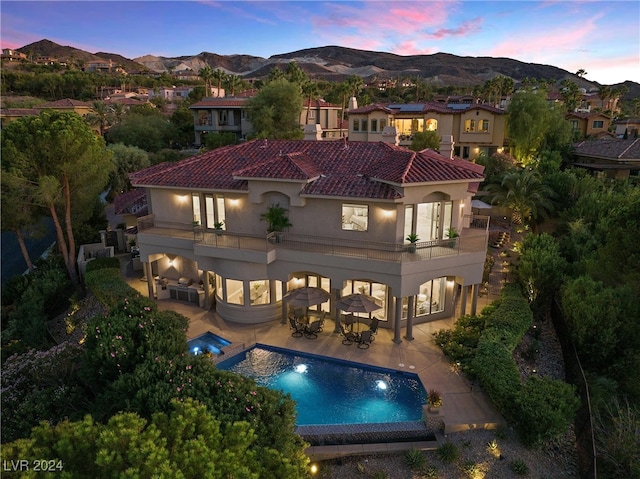 back house at dusk featuring a patio area, a mountain view, and a balcony