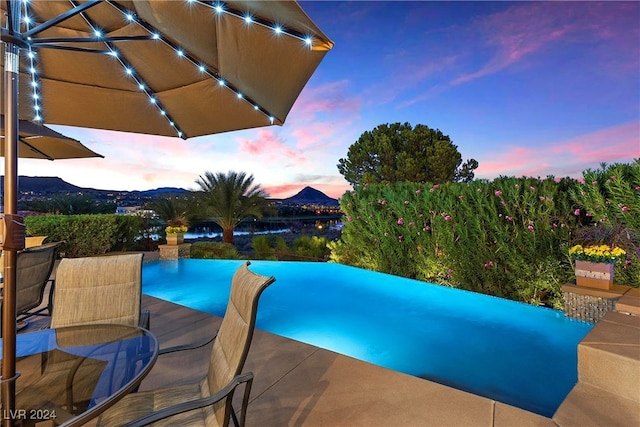 pool at dusk featuring a patio and a water and mountain view