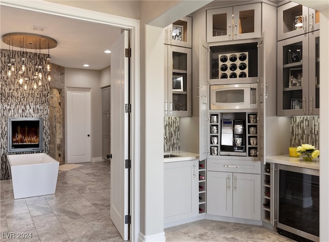 bar with decorative backsplash, stainless steel microwave, wine cooler, and gray cabinetry