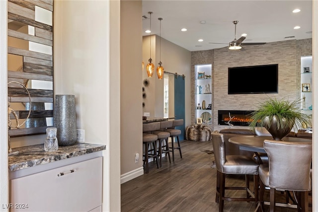 dining room featuring a barn door, ceiling fan, a fireplace, and dark hardwood / wood-style flooring