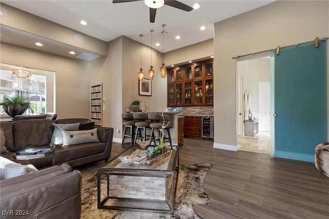 living room with bar area, a barn door, ceiling fan, dark wood-type flooring, and wine cooler