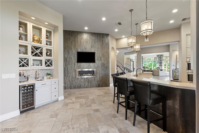 bar with tasteful backsplash, beverage cooler, a fireplace, decorative light fixtures, and white cabinets