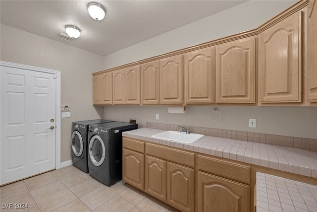 laundry area with cabinets, light tile patterned flooring, separate washer and dryer, sink, and a textured ceiling