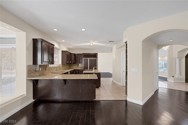 kitchen featuring a breakfast bar, kitchen peninsula, dark brown cabinets, wood-type flooring, and decorative backsplash