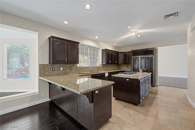 1931 Fox Canyon Cir, Las Vegas, NV 89117 - kitchen featuring dark brown cabinets, baseboards, light stone counters, a peninsula, and tasteful backsplash