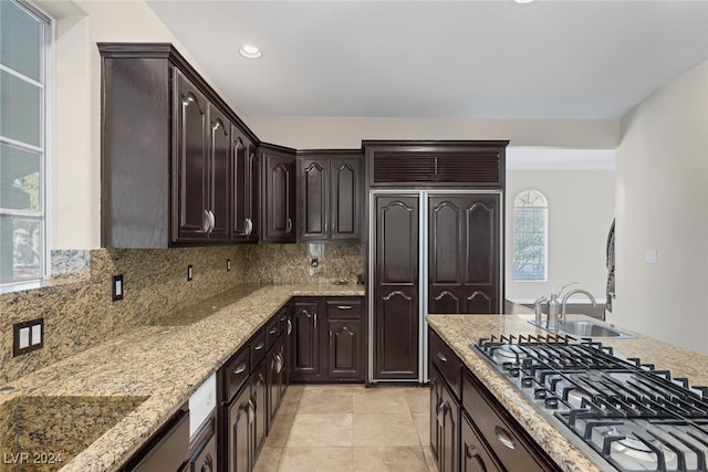 kitchen featuring stainless steel gas stovetop, light stone counters, tasteful backsplash, paneled fridge, and dark brown cabinets