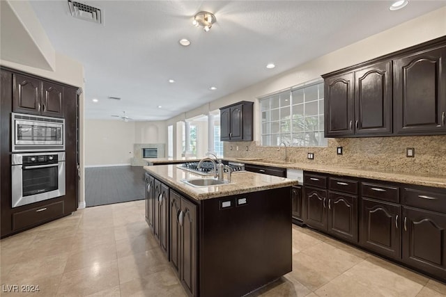 1931 Fox Canyon Cir, Las Vegas, NV 89117 - kitchen with appliances with stainless steel finishes, a center island with sink, a sink, light stone countertops, and decorative backsplash