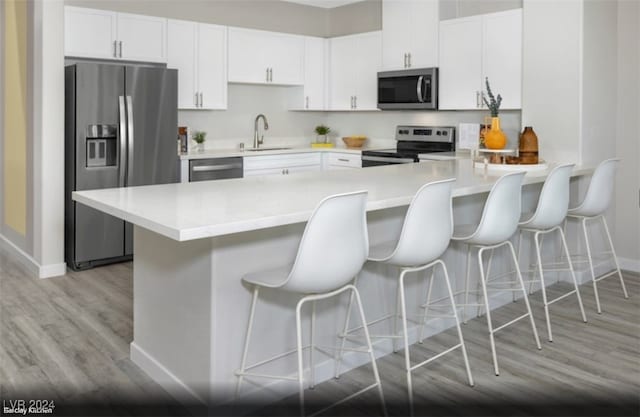 kitchen with sink, a breakfast bar, light wood-type flooring, white cabinetry, and appliances with stainless steel finishes