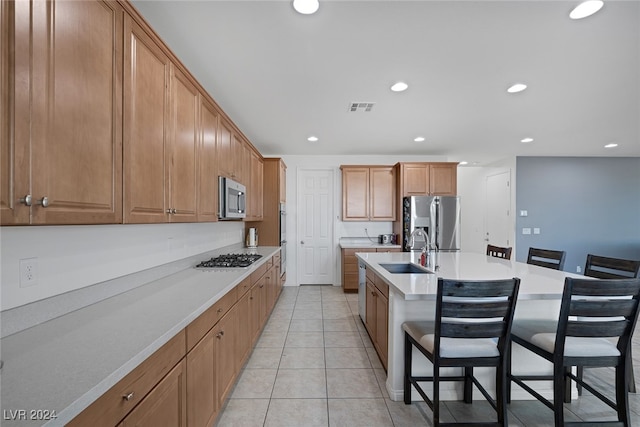 kitchen with a center island with sink, a breakfast bar area, light tile patterned flooring, sink, and stainless steel appliances