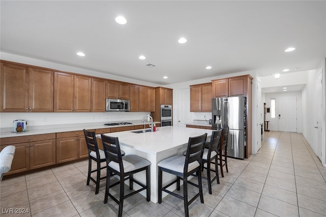 kitchen with a breakfast bar area, a center island with sink, sink, light tile patterned flooring, and appliances with stainless steel finishes