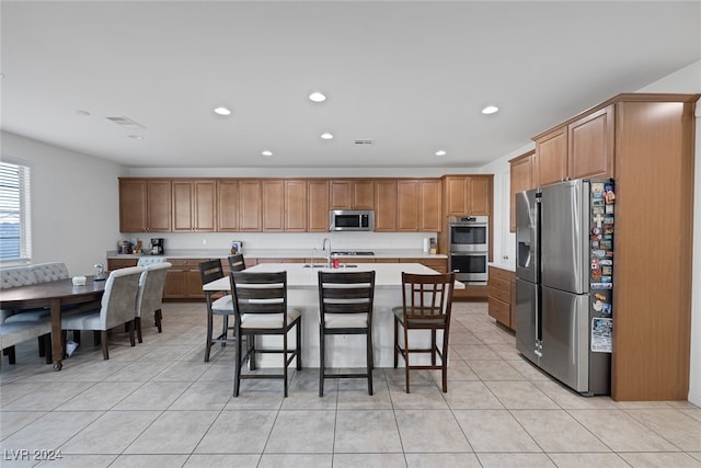 kitchen featuring a center island with sink, appliances with stainless steel finishes, a breakfast bar, light tile patterned flooring, and sink